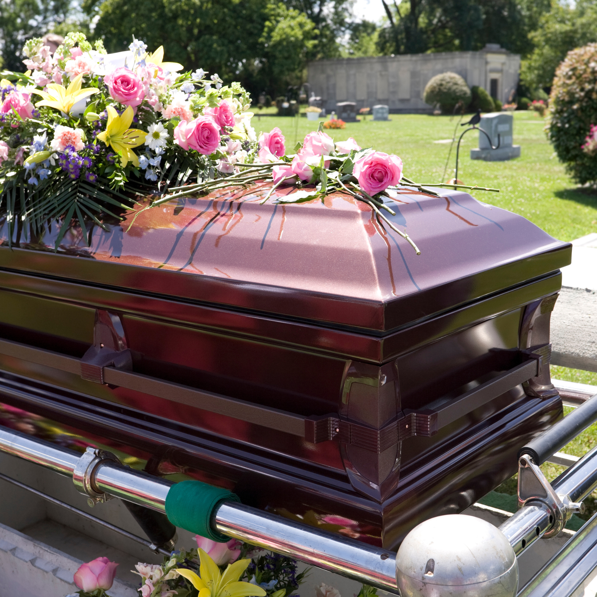 Photo of a polished casket topped with large bouquets of flowers.