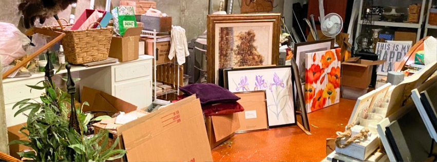 A very cluttered image of a basement full of various things including artwork, furniture, throw pillows, and storage containers.