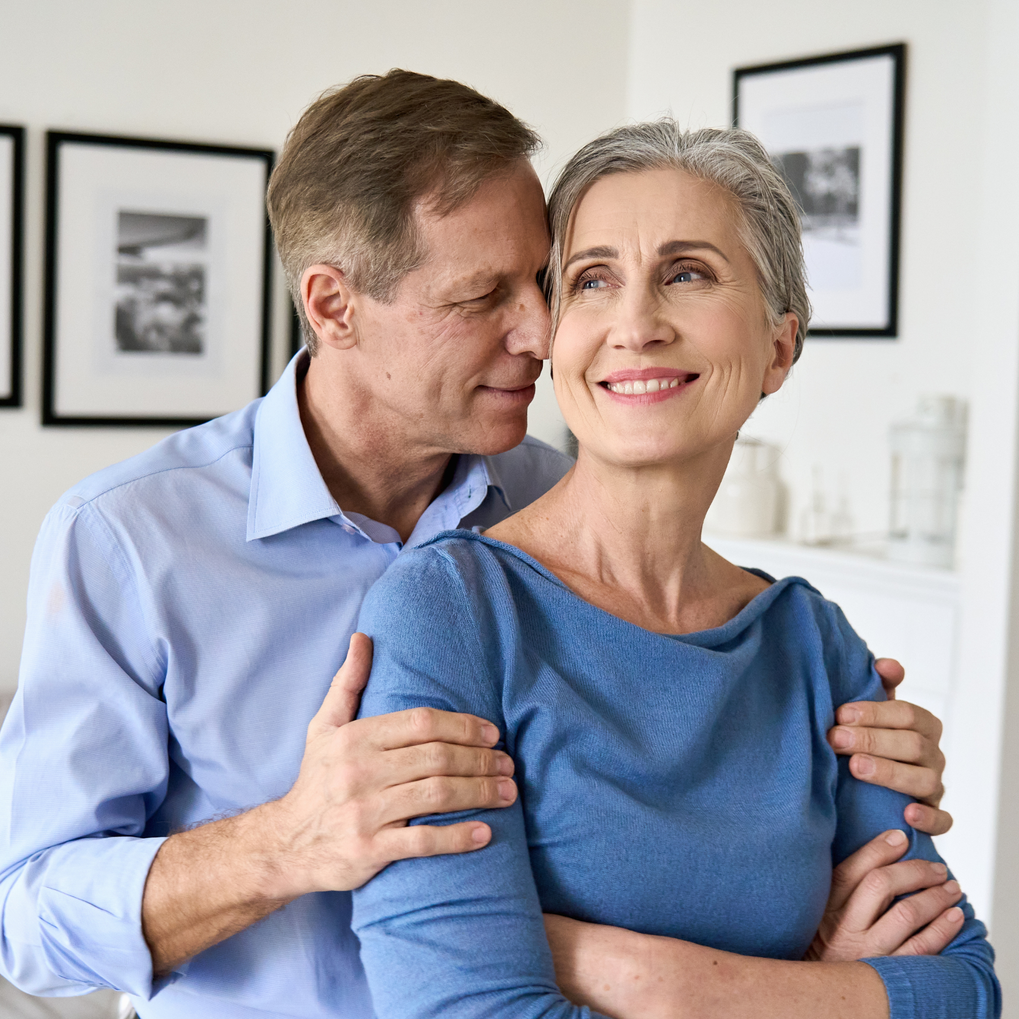 A middle-aged or older couple embraces in a living room. They are happy and in love.