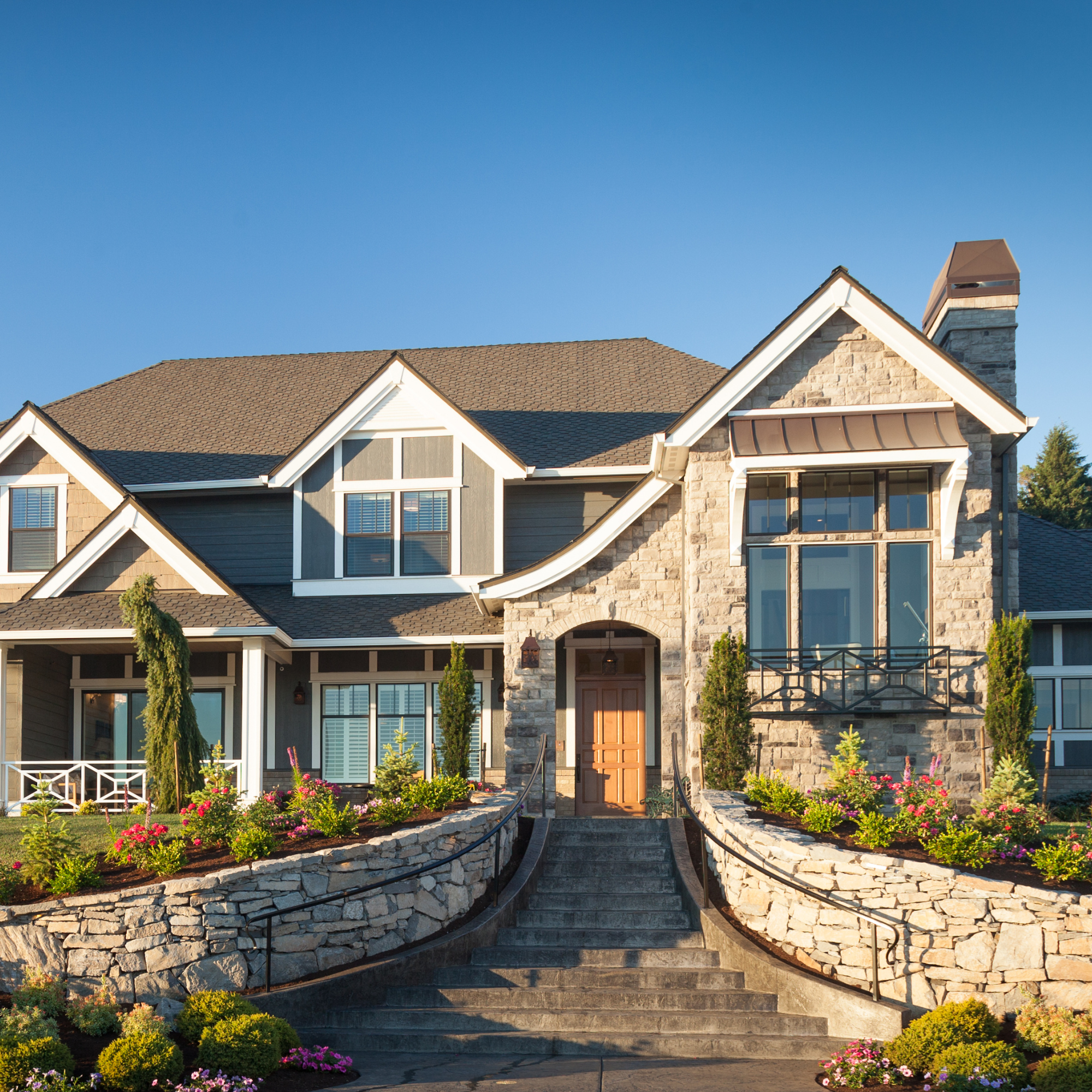 A photo of a large, luxurious contemporary stone home with a curved, walled staircase leading up to the front door.